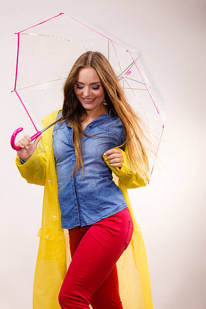Woman rainy smiling girl wearing waterproof yellow coat standing under umbrella having fun. Meteorology, forecasting and weather season concept