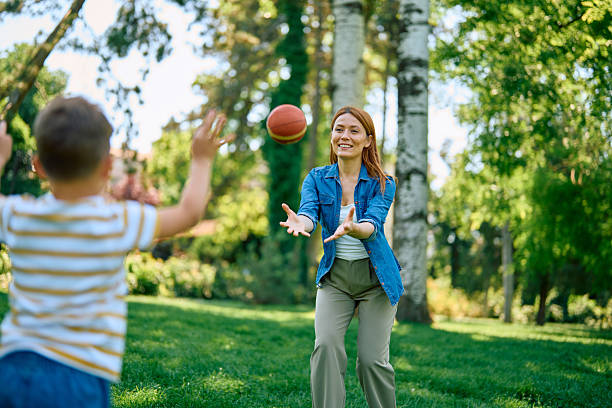 Happy mother and son playing together with a ball in the park on a sunny day, relishing quality time, fostering joy, and creating cherished memories amidst nature's beauty