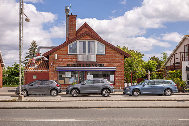 Amager, Copenhagen, Denmark - May 30th 2025: This image showcases a villa on Kongelundsvej in the Amager suburb of Copenhagen that has been converted into a pizzeria. The building features a combination of traditional residential architecture and commercial signage, indicating its new purpose. A hedge partially surrounds the property, providing a touch of greenery, while a paved walkway leads to the entrance. The signage and outdoor elements reflect a blend of home-like charm and a welcoming business atmosphere, illustrating the adaptive reuse of residential spaces for commercial purposes. The scene is framed by an overcast sky, casting soft, diffused lighting over the setting.