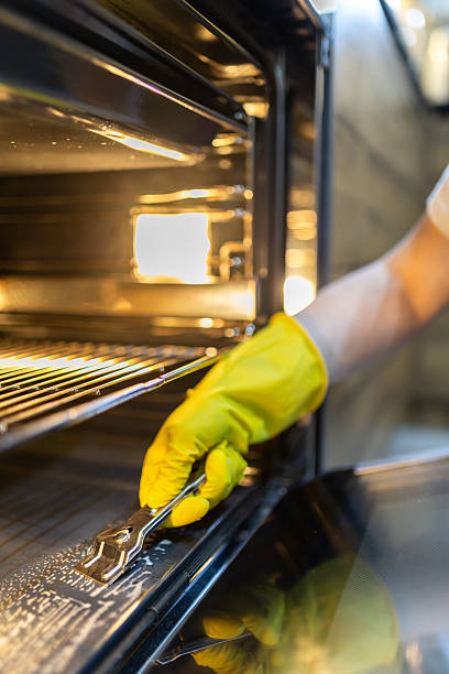istock Cleaning an oven with a yellow glove while using a tool to scrape off residue 2218453849