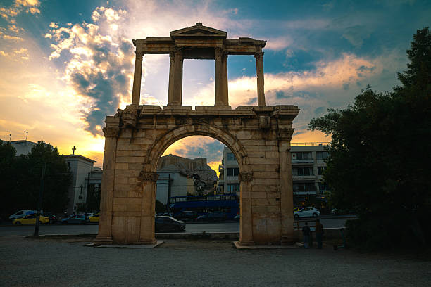 Hadrian’s Arch stands tall at sunset in the heart of Athens, Greece. This iconic Roman structure, built in the 2nd century AD, creates a visual contrast between classical antiquity and the modern city seen through its central arch. The golden hues of the evening sky emphasize the marble textures and historic grandeur of the monument. This image is ideal for travel publications, historical features, educational use, or editorial content highlighting cultural heritage, architectural legacy, or the timeless beauty of ancient structures in urban environments.
