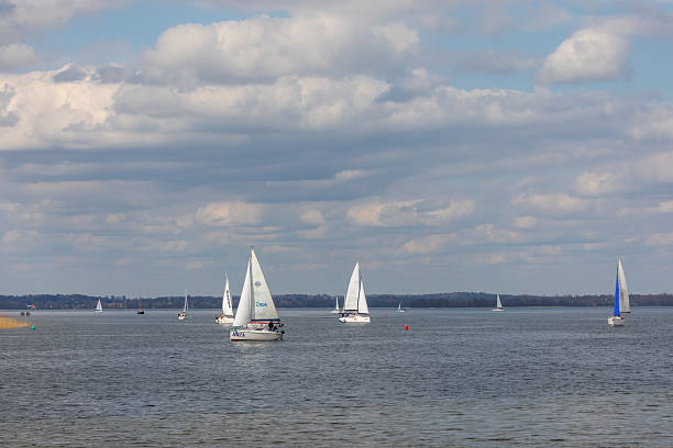 Rydzewo, Poland - May 01, 2021: White and blue sailing boats during a regatta on Mazury lakes under cloudy skies.