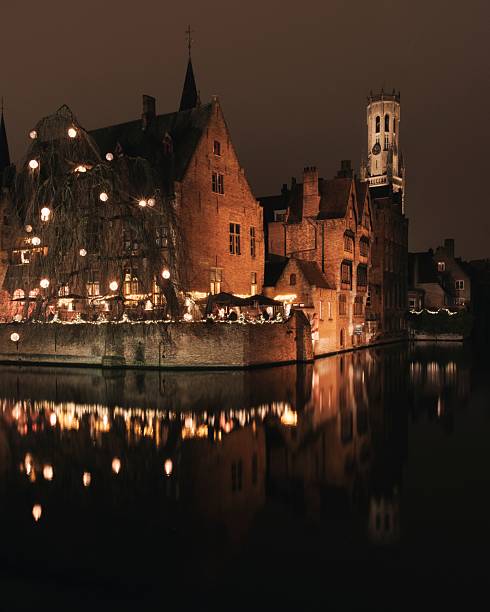 Night view of Bruges with illuminated medieval buildings and reflections in the canal, creating a serene and enchanting atmosphere.
