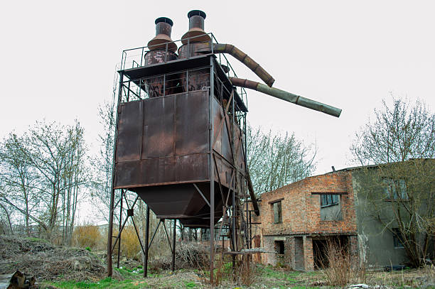 istock Rusty structure towers over wild grass and trees in an abandoned industrial site, showcasing a forgotten era of manufacturing and decay 2218460359