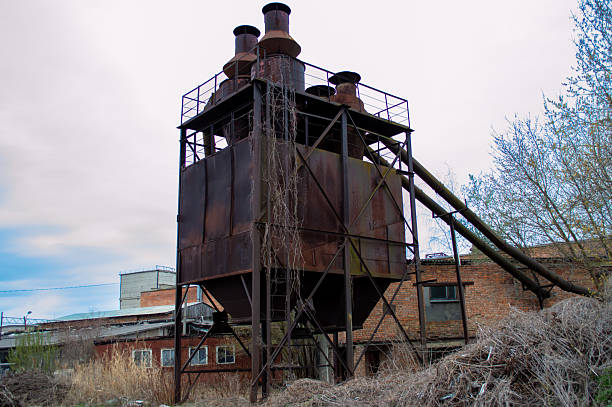 Large rusted industrial structure stands neglected with vines growing, showcasing the remnants of a once-busy factory environment.