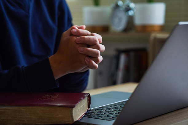istock Christian online technology concept. Hands praying of christian with digital computer laptop, Online live church for sunday service. Asian catholic man are reading Holy bible book and online study. 2218460651