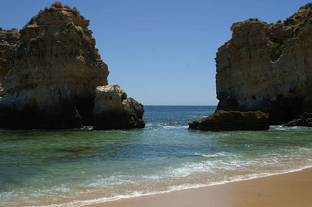 Breathtaking view of the Algarve coastline in Portugal, where golden cliffs meet the sparkling Atlantic. The rugged rocks and crystal-clear waters create a stunning natural landscape, perfect for travel magazines, vacation brochures, and nature-themed projects. A serene and inspiring coastal escape under a soft summer sky.