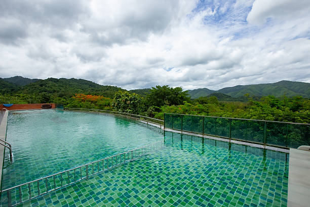 A peaceful infinity pool with vibrant blue mosaic tiles reflects the cloudy sky above, evoking a sense of calm and relaxation