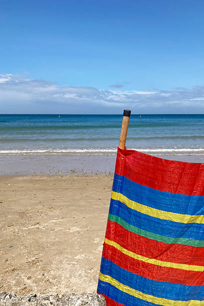 istock Bright coloured windbreak erected on the beach providing wind protection for holiday makers - looking to enjoy a day on a beautiful beach. Sea in the distance 2218469123