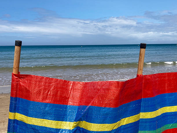 istock Bright coloured windbreak erected on the beach providing wind protection for holiday makers - looking to enjoy a day on a beautiful beach. Sea in the distance 2218469152