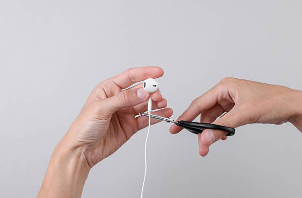 istock Female hands cutting wired headphones with scissors on gray background 2218470932