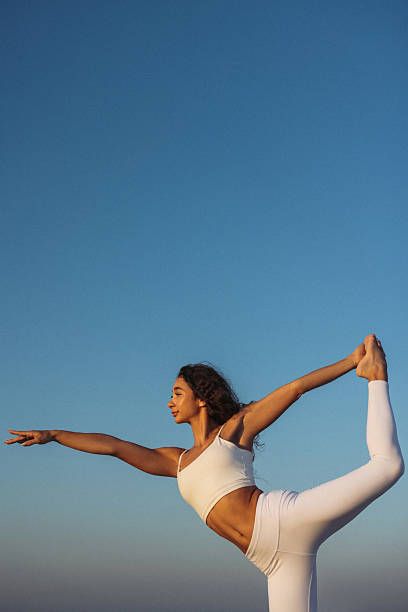 A serene moment of a woman in white activewear performing a yoga pose outdoors under a clear evening sky. The environment conveys a sense of calmness, focus, and physical wellness. Ideal for themes of fitness, mindfulness, and outdoor activities.