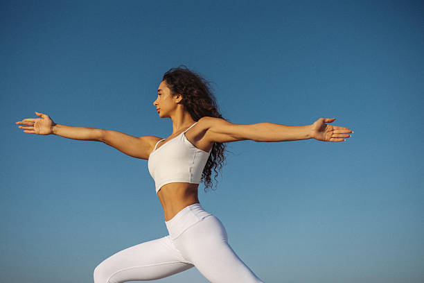 istock Woman Practicing Yoga Outdoors in a Warrior Pose Under Bright Clear Sky 2218475709