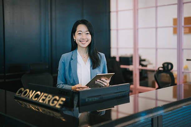 istock Confident Asian woman smiling at Reception Desk Using Digital Tablet 2218477885