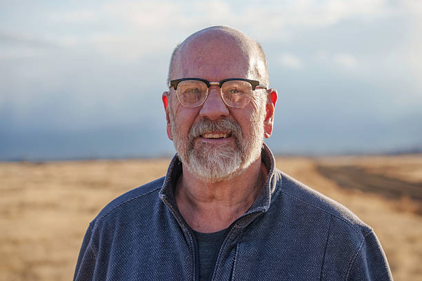 istock Elderly Man Stands in Rural Landscape Under Winter Sun, Facing Camera Calmly 2218479641