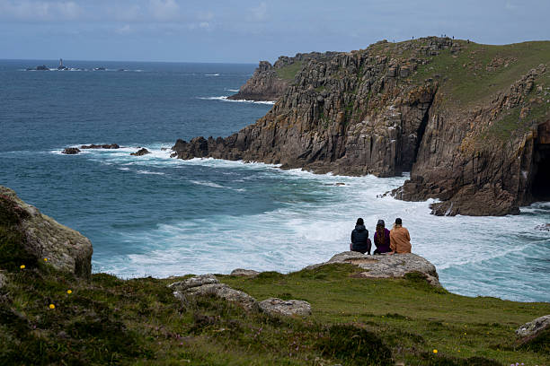 Friends sit on rock headland above ocean and cliffs, Cornwall