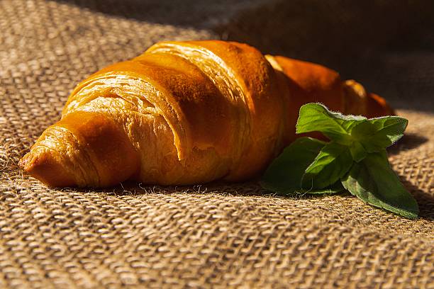 istock Golden croissant on rustic burlap with mint sprig, natural light 2218483296