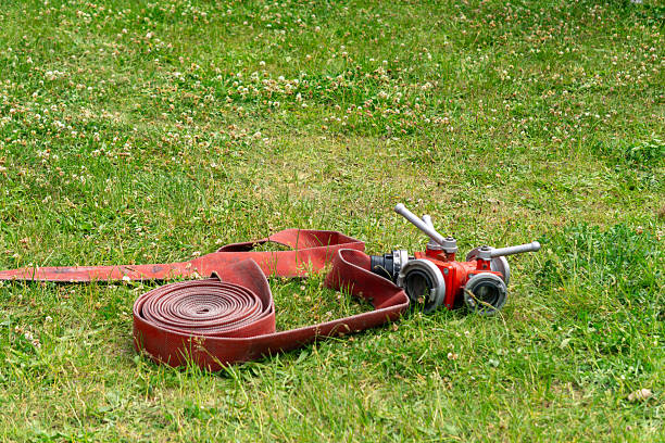 red fire hose splitter with a coiled fire hose lying on green grass. Equipment used during firefighting operations