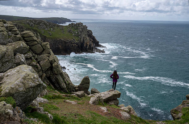istock Young woman stands on rock above ocean 2218485406