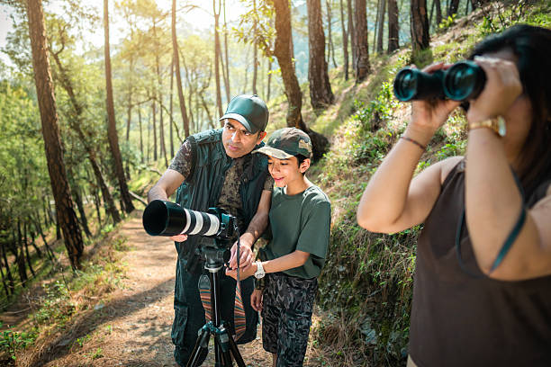 istock Father teaches his son to use a camera on a tripod, while his mother spots birds with binoculars on a forest trail. 2218486145
