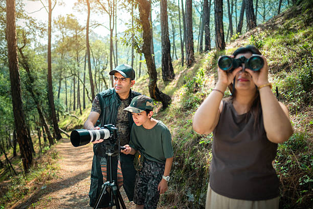 istock Father teaches his son to use a camera on a tripod, while his mother spots birds with binoculars on a forest trail. 2218486150