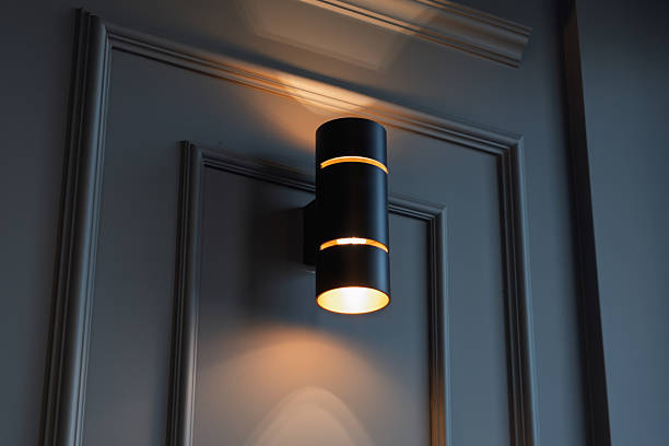 istock Modern black cylinder wall sconce illuminates a dark panelled wall, creating a warm upward and downward glow with soft shadows and elegant lines. 2218488182