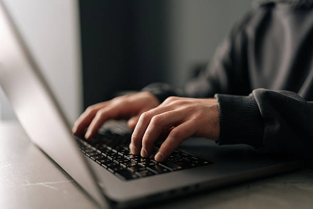 istock Close-up hands of unrecognizable programmer male typing on laptop keyboard, immersed in software development or coding, sitting at table by window in dark room. 2218490189