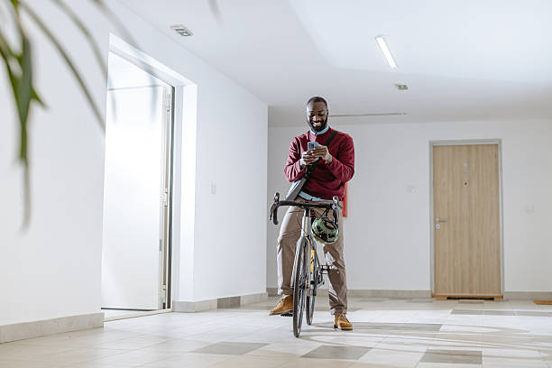 istock Man in modern hallway texting on phone while standing beside bicycle 2218490491