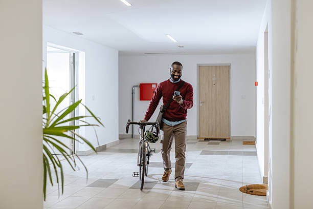 istock Man in modern hallway texting on phone while standing beside bicycle 2218490534