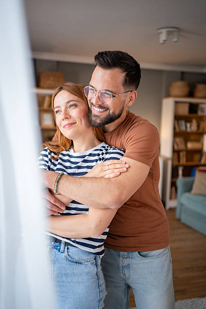 istock Happy young couple embracing at home looking out the window 2218499152