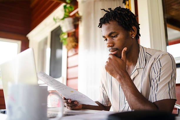 istock Home office professional reviewing paperwork, concentrating intently while managing remote work on personal laptop 2218500339