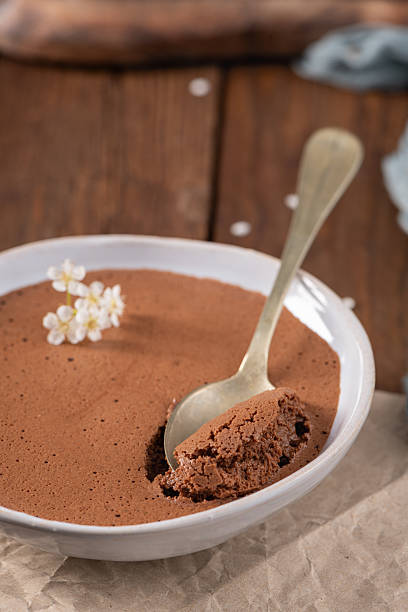 istock Silky chocolate mousse in a white bowl, a spoonful being lifted, decorated with tiny white flowers, presented on crumpled parchment paper and a rustic wooden table 2218502063