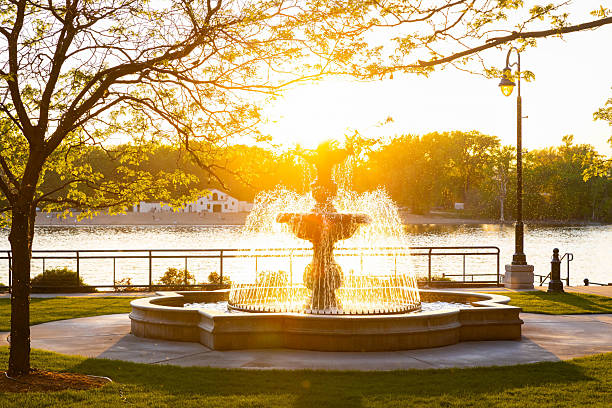 A scenic view of the fountain at La Crosse Riverside Park, with golden sun beams streaming through the dusky sky, creating a serene and peaceful atmosphere.