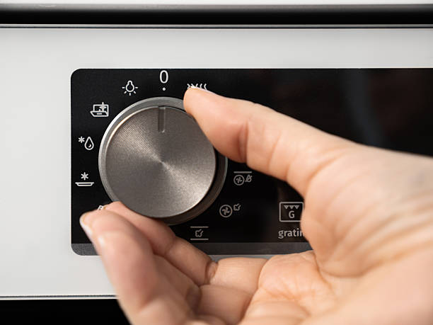 istock Woman adjusting modern white oven in kitchen.  Female hand pushing and turning knobs on oven control panel 2218507764