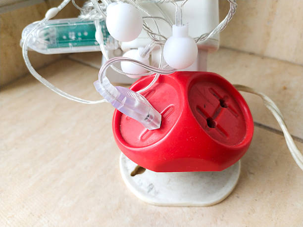 istock A closeup showcasing a red, cubeshaped adapter plugged into a wall socket, powering decorative string lights. Represents electricity, connection, and domestic life. 2218510143