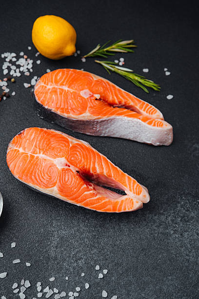 istock Fresh salmon fillets with lemon and herbs on dark stone background 2218510560