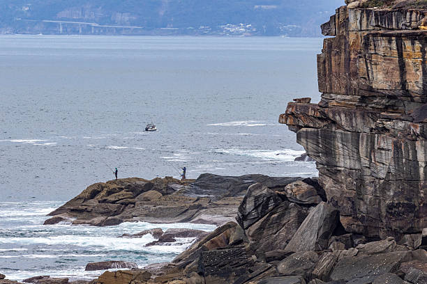 Fishermen on the shore below sandstone cliffs in the Royal National Park, Sydney Australia