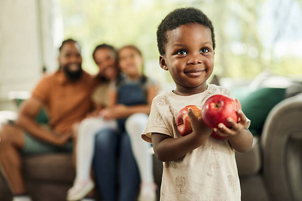 Cute African American boy holding apples at home. His family is in the background.