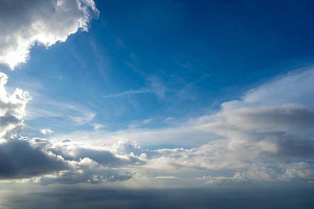 Majestic clouds illuminated by the sun create a dramatic sky viewed from above. The bright sunlight contrasts with the deep blue sky and shadowed clouds