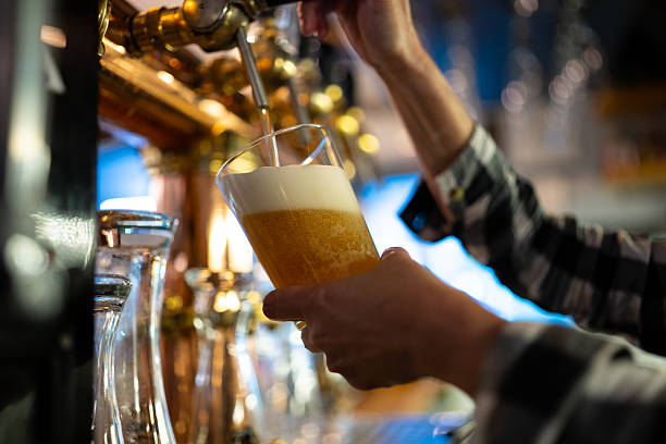 istock Bartender pouring fresh draft beer into glass from tap at bar with soft lighting 2218557230