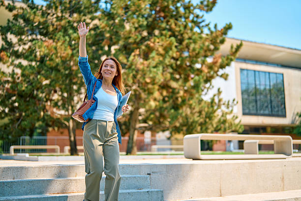 istock Cheerful teacher waving while walking down the stairs in university campus 2218558242