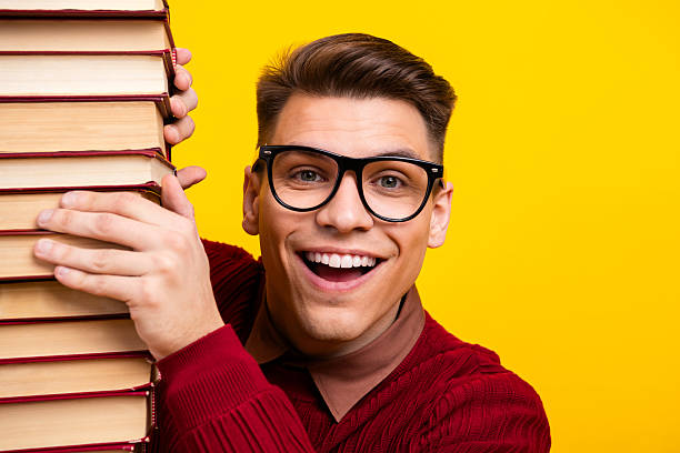 istock Smiling Intelligent student Young Man Holding Stack of book Against Yellow Background 2218559228