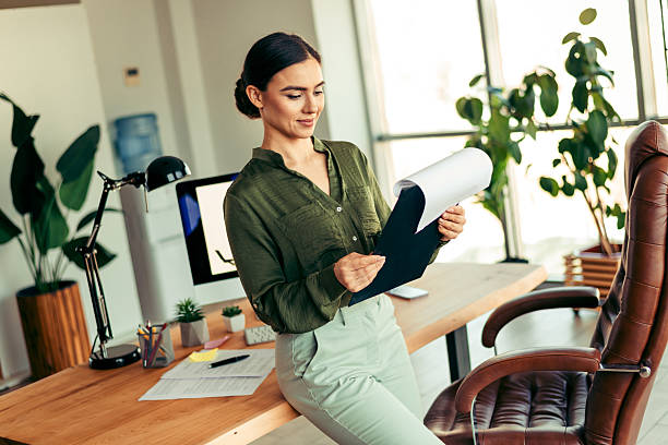 istock Elegant businesswoman analyzing documents in a modern office setting with natural light and stylish workplace decor 2218559529