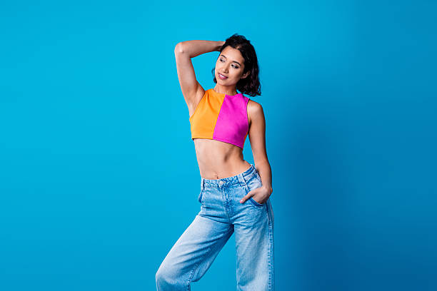 istock Confident young woman in vibrant fashion posing confidently against a solid blue background, radiating happiness and charm. 2218564659
