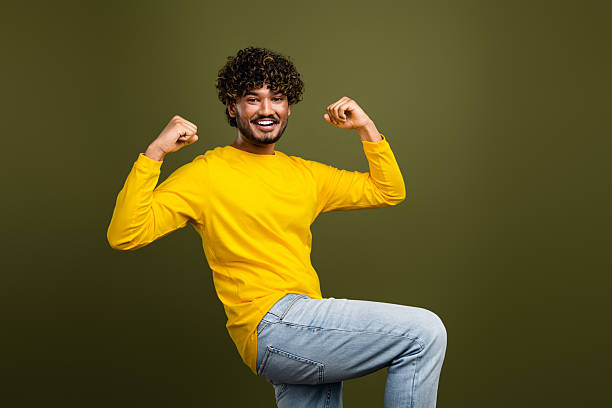 istock Smiling man in vibrant yellow sweater posing confidently with a dynamic gesture on a solid khaki green background 2218566868