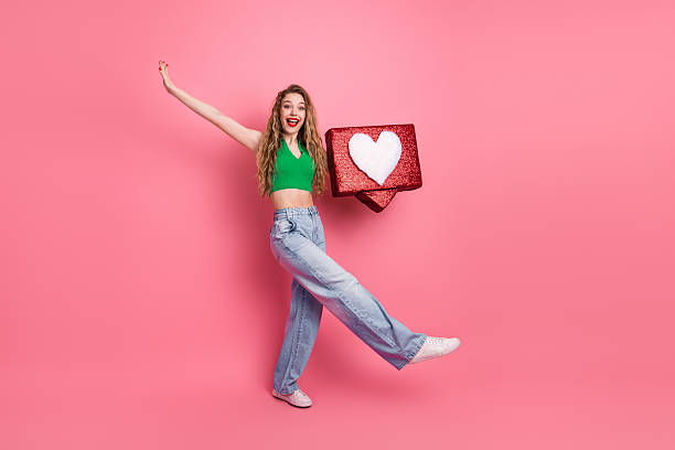 istock Young woman joyfully posing with gift box on bright pink background, expressing happiness and style in trendy attire 2218567713