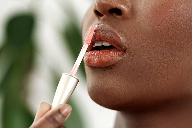 istock Woman applying lip gloss in a natural setting with greenery in the background during daylight hours 2218577370