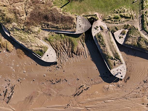 Aerial view of beached concrete ships on a muddy shore, surrounded by grass and sand, showcasing unique coastal landscape.