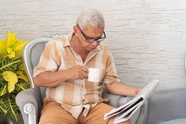 Relaxed senior man enjoying his morning coffee while reading the newspaper in an armchair at home