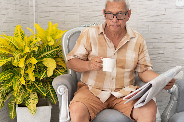 Relaxed senior man enjoying his morning coffee and reading the newspaper in a comfortable armchair at home